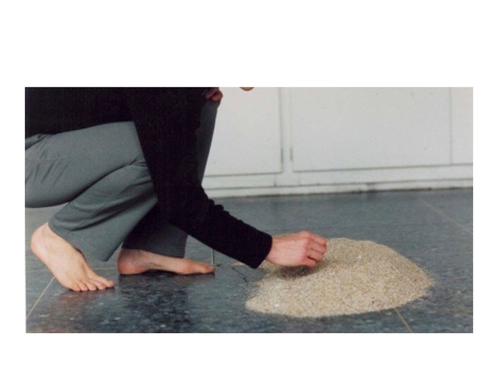 a white woman squatting down by a pile of sand, two bare feet right hand visible